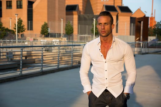 Handsome muscular blond man standing in city setting looking to a side, large copyspace