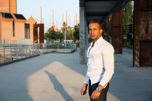Handsome muscular blond man standing in city setting looking at camera, large copyspace