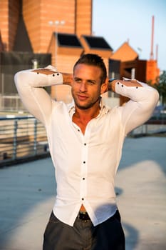 Handsome muscular blond man standing in city setting looking to a side smiling
