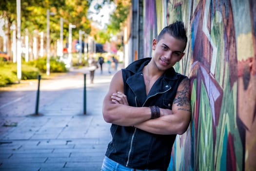Handsome young man leaning against colorful graffiti wall, smiling at camera