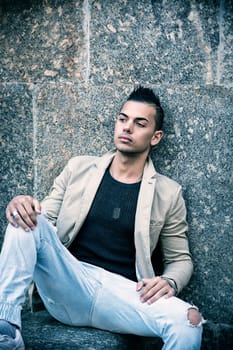 Attractive young man in urban setting, sitting on marble steps in city square looking away