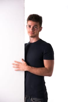 Attractive young man or teenager standing next to blank white display, large copy-space
