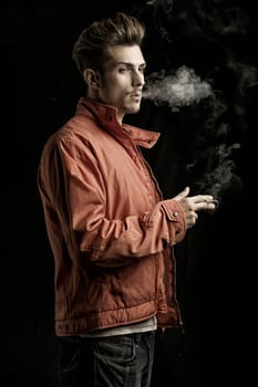 Handsome young man smoking cigarette, dressed as James Dean with red jacket on dark background