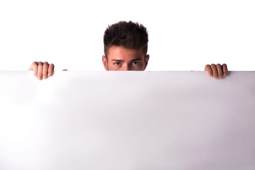 Attractive young man or teenager peeking over blank white display, large copy-space