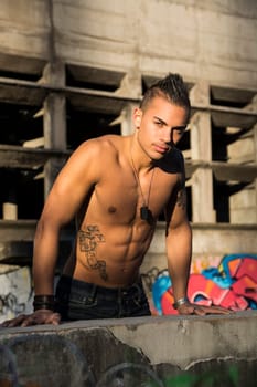 Handsome fit athletic shirtless young man in city setting balancing on concrete wall