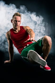 Athletic trendy handsome fit young man in a hat doing a break dance routine, smoke and black background behind