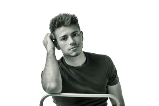 Attractive young man sitting, leaning on back of a chair looking at camera, isolated on white, black and white shot