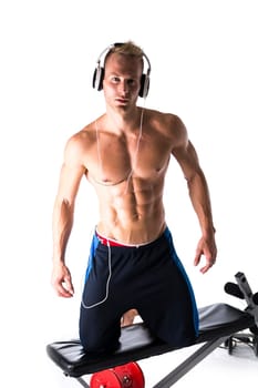 Muscular shirtless young man exercising with weights, bench, dumbbells, listening to music, isolated on white