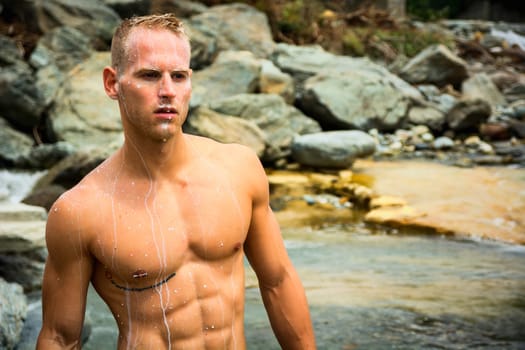 Handsome young muscle man standing in water pond, naked with milk dripping from his body