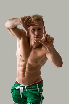Handsome blond muscular shirtless young man doing frame gesture with fingers, looking at camera through it