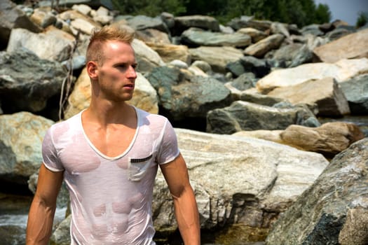Handsome young muscle man standing, wearing wet white t-shirt, looking to a side. Large copyspace
