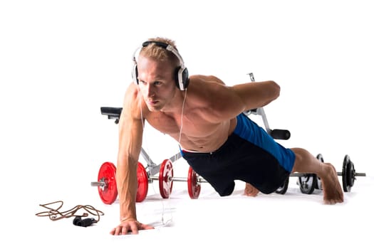 Muscular shirtless young man exercising with weights, bench, dumbbells, listening to music, isolated on white