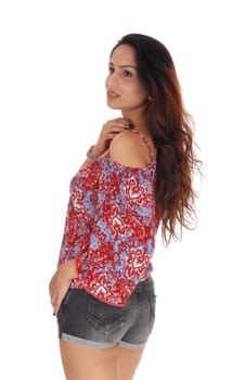 A slim young woman standing in shorts and colorful blouse from the.back, looking over her shoulder, isolated for white background.
