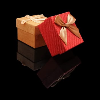 Two closed gift box paper and fabric texture with a bow on a black glossy background with real reflection. Isolated.