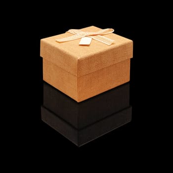 Gift box close fabric texture beige with a bow on a black glossy background with real reflection. Isolated.