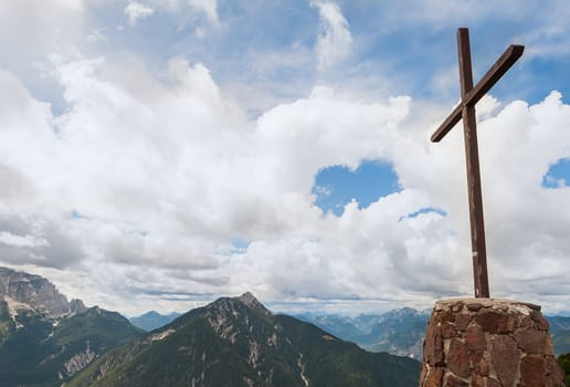 Wooden cross on top of the mountain. Mountain landscape above the clouds. Cross on top of a mountain peak as typical in the Alps.