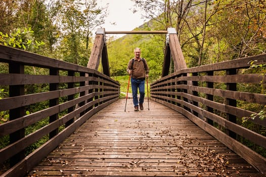 Mature man are hiking in the mountains, walking on a wooden bridge