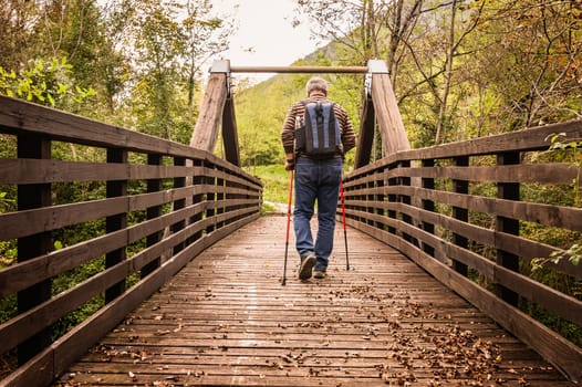 Mature man are hiking in the mountains, walking on a wooden bridge