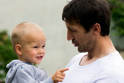 Boy and his uncle are outdoors. The little boy shows to something.