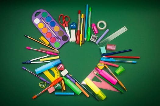 Different school supplies in heart shape on green background.