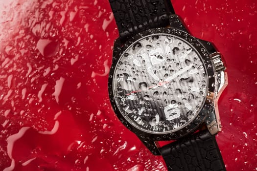 Wet water proof wrist watch for men is on red background with water drops.