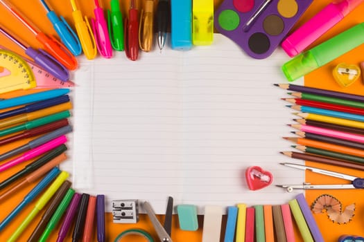 Different school supplies are on white blank notebook.