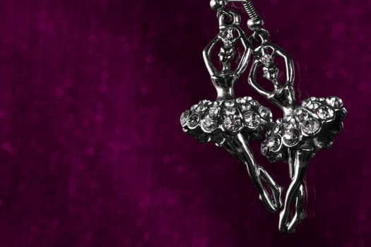 Silver earrings from ballerina shape on dark purple background.