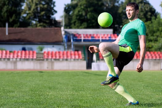 The football player is practicing shoots with the ball on playing field.