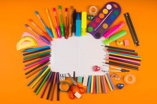 Different colorful school supplies on notebook on orange background.