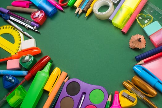 Different colorful school supplies are on green background.