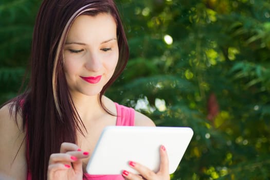Young smiling woman with white digital tablet in nature.