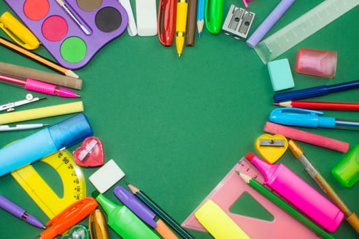 Different colorful school supplies in heart shape on green background.