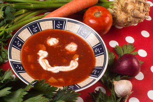 Smiling tomato soup with organic vegetables on red background.