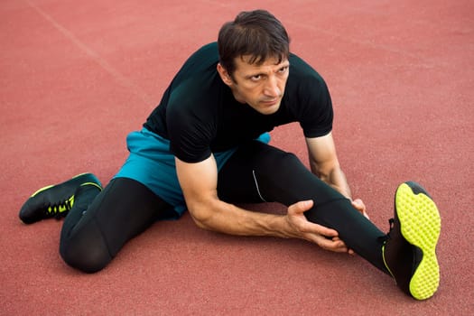 The athlete sportsman is stretching his legs outdoors.