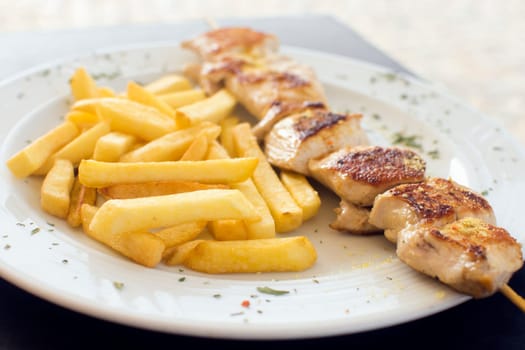 Chicken meat on spit and french fries or baked potato on white plate.