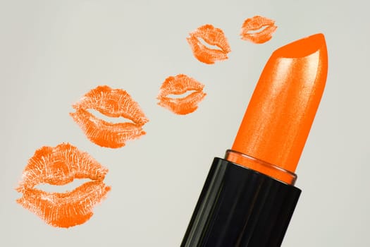 Orange lipstick and orange lipstick kisses are on gray background.