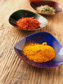 Assortment of different spices in colorful copper bowls on a rustic wooden table