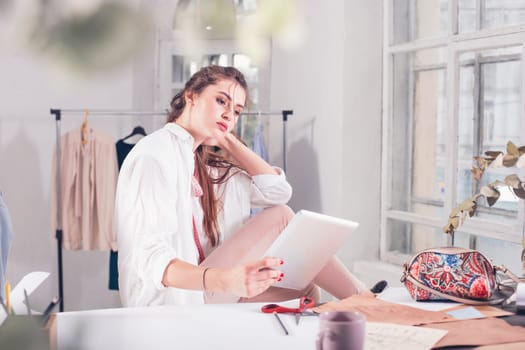 The female fashion designer working in studio sitting on the desk