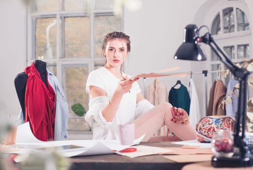 The female fashion designer working in studio sitting on the desk
