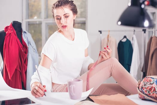 The female fashion designer working in studio sitting on the desk