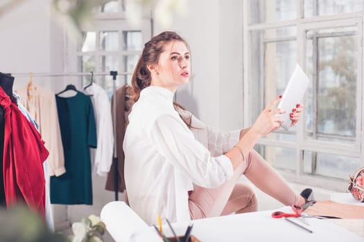 The female fashion designer working in studio sitting on the desk