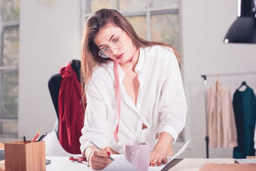 The female fashion designer working in studio sitting on the desk