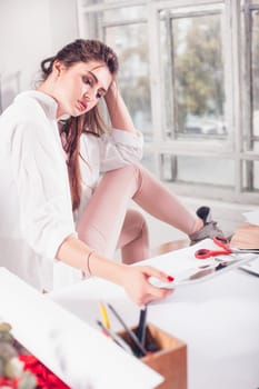 The female fashion designer working in studio sitting on the desk