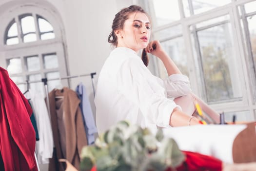 The female fashion designer working in studio sitting on the desk