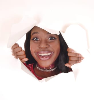 A beautiful happy African woman looking smiling through a hole in a.paper, with mouth open, isolated for white background.