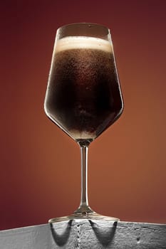 The glass of cold frothy dark beer on an old wooden table