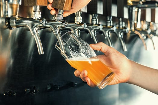 Hand of bartender pouring a large lager beer in tap. Soft, vintage instagram effect on photo