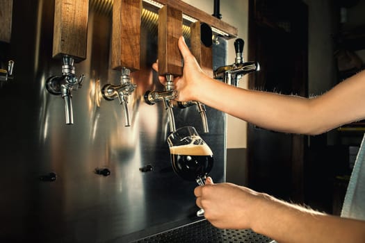 Hand of bartender pouring a large lager beer in tap. Soft, vintage instagram effect on photo