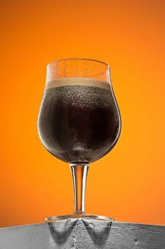 The glass of cold frothy dark beer on an old wooden table against colored background