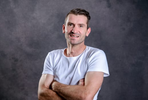 friendly young man with crossed arms in front of gray background